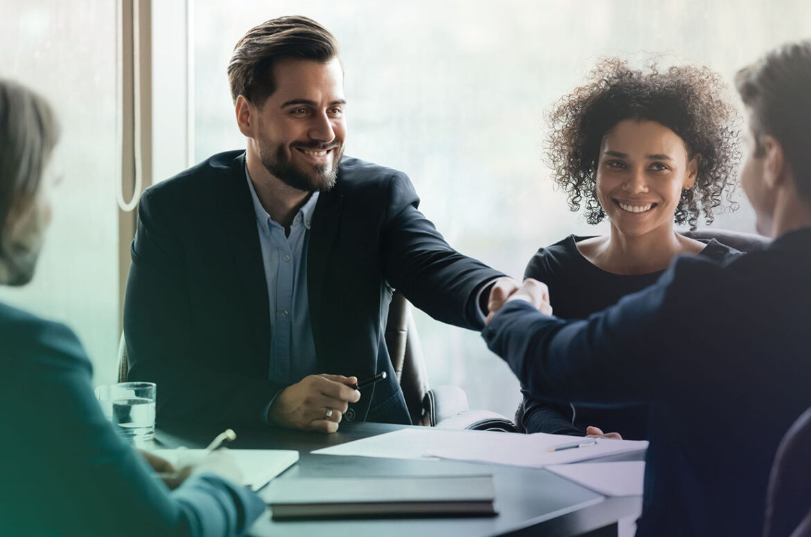 Independent insurance agency business owners are sitting at a table conducting business and shaking hands.