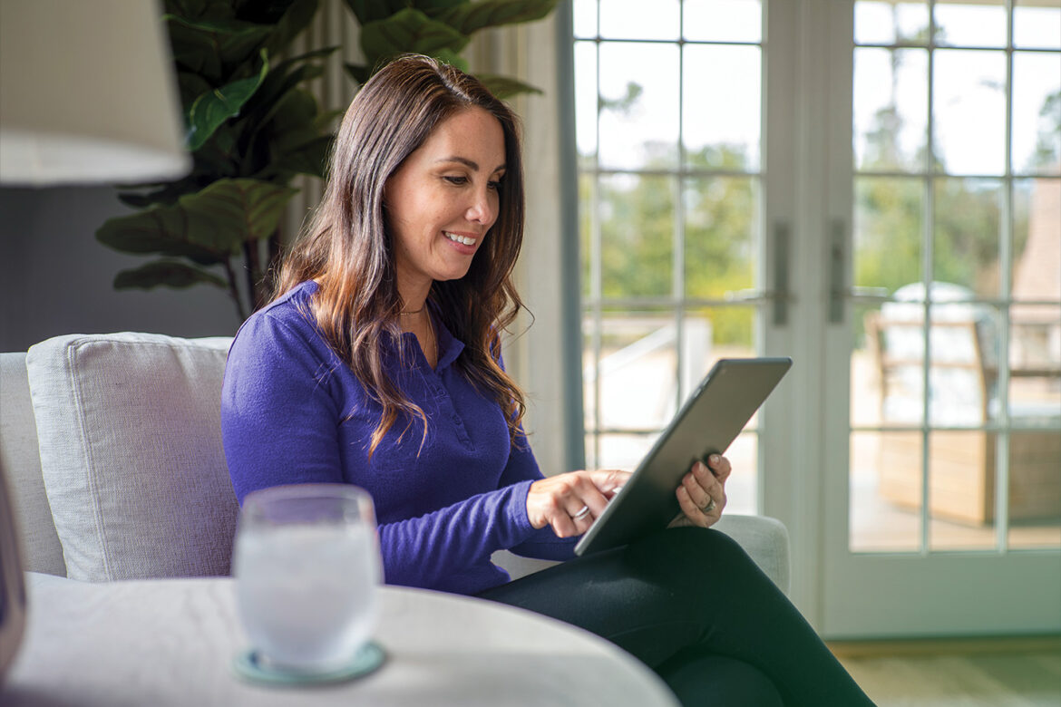 Female sitting casually in her home living room looking at personal high-yield savings account options on her tablet